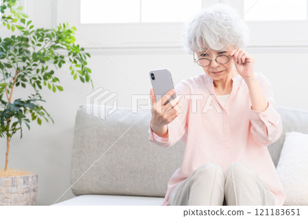 Senior woman struggling to see her smartphone due to presbyopia 121183651