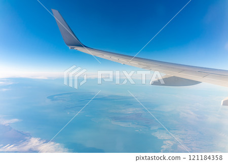 View from the airplane window at a beautiful blue clear sky, earth, sea and the airplane wing 121184358