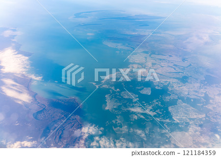 View from the airplane window at a beautiful blue clear sky, earth, sea and the airplane wing 121184359