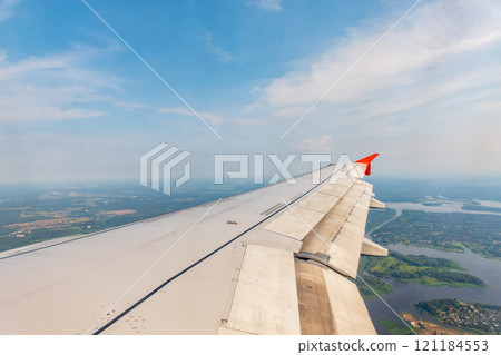 View of airplane wing, blue skies and green land during landing. Airplane window view. 121184553