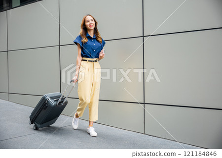 Businesswoman using mobile phone app in airport lounge while waiting for her flight, with stylish luggage and travel accessories. Asian traveler on business trip using smartphone app at airport. Businesswoman using mobile phone app in airport lounge while waiting for her flight, with stylish luggage and travel accessories. Asian traveler on business trip using smartphone app at airport. 121184846