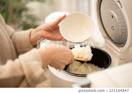 一位中年婦女晚上在廚房裡把剛煮好的米飯從電鍋裡倒進碗裡 121184847