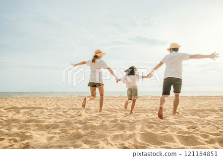 Happy Asian parents with their daughters enjoying playful at beach. Little girls with their mother and father holding hand of child running and pretending on sand. Positive family outdoor activity 121184851