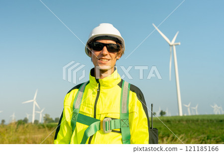 Close up and portrait of wind turbine worker or engineer man stand and look at camera with smiling also row of wind turbine pole in the background. 121185166