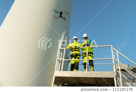 Wide shot two wind turbine or windmill workers or engineer stand on base of the pole and one control drone with discuss together in workplace field. 121185176