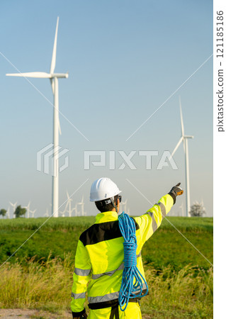 Vertical image of back of wind turbine or windmill engineer worker point to his right side with row of wind turbine in the background. Vertical image of back of wind turbine or windmill engineer worker point to his right side with row of wind turbine in the background. 121185186