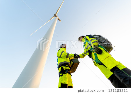 Two of wind turbine or windmill workers or technician shake hands and stand on base of wind turbine. Two of wind turbine or windmill workers or technician shake hands and stand on base of wind turbine. 121185211