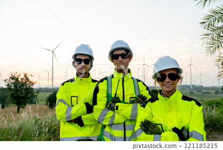 Portrait group of wind turbine workers or technicians stand with arm crossed and look at camera with row of wind turbine in the background. Portrait group of wind turbine workers or technicians stand with arm crossed and look at camera with row of wind turbine in the background. 121185215