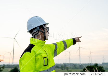 Portrait of wind turbine worker or technician man stand with point to his left side with row of wind turbine in the background. 121185218