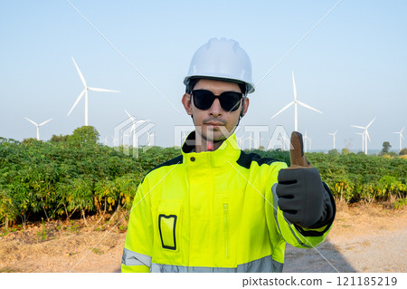 Portrait of wind turbine worker or technician man stand with show thumbs up and look at camera with row of wind turbine in the background. 121185219