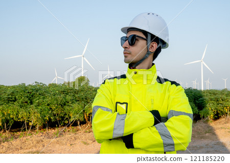 Portrait of wind turbine worker or technician man stand with arm-crossed  and look to his right side with row of wind turbine in the background. 121185220