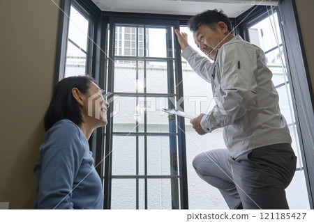 A woman asking a contractor to repair a window sash 121185427