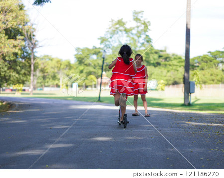 Cute sisters riding scooters on a sunny summer day in the park. Active leisure and outdoor sport for child. 121186270
