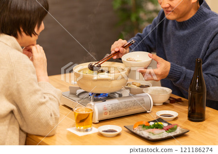 A middle-aged couple enjoying hot pot dinner in the living room on a winter night 121186274