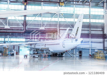 Passenger aircraft under maintenance. Checking mechanical systems for flight operations. White jet plane in the hangar 121186409