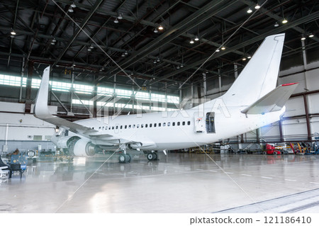 White jet plane in the hangar. Checking mechanical systems for flight operations. Passenger aircraft under maintenance White jet plane in the hangar. Checking mechanical systems for flight operations. Passenger aircraft under maintenance 121186410