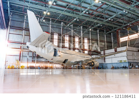 White passenger airplane in the hangar at the morning light. Checking mechanical systems for flight operations. Aircraft under maintenance 121186411