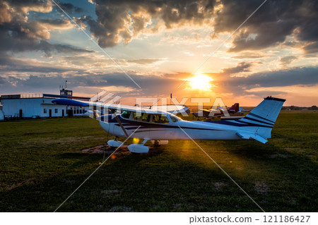 Small private airplanes on the airfield against the backdrop of a colorful sunset 121186427