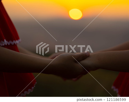 Two little girls holding hands on a summer sunset background. Family love with colorful sunset. 121186599
