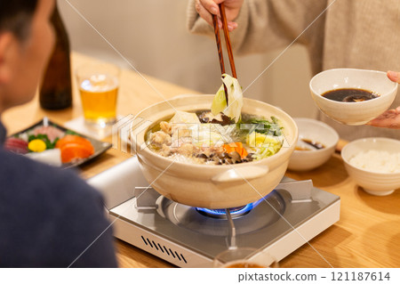 A middle-aged couple enjoying hot pot dinner in the living room on a winter night 121187614
