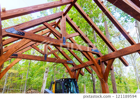 Solid wooden frame is being built for gazebo among tall trees, greenery, showcasing skilled craftsmanship. 121189594