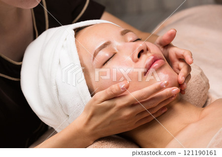 A young Asian woman is getting a facial massage. A young Asian woman is getting a facial massage. 121190161
