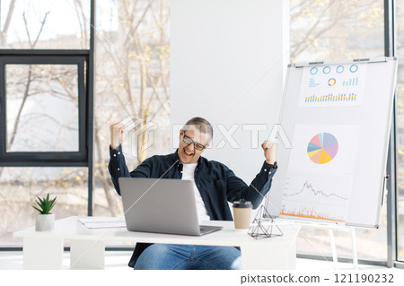 A man dressed in casual clothes works in the office with a laptop and expresses positive emotions A man dressed in casual clothes works in the office with a laptop and expresses positive emotions 121190232