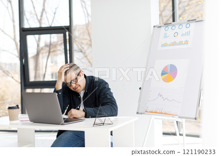 A man dressed in casual clothes works in the office with a laptop and expresses sad emotions. A man dressed in casual clothes works in the office with a laptop and expresses sad emotions. 121190233