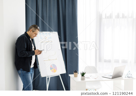 A man dressed in casual clothes works in the office and holds a mobile phone 121190244
