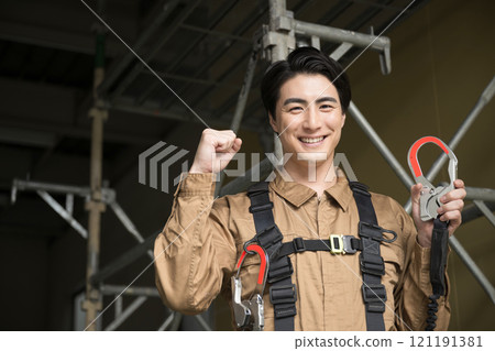 Smiling worker wearing safety belt and posing with fist pump, looking at camera. Image of blue collar worker job change or job offer. Smiling worker wearing safety belt and posing with fist pump, looking at camera. Image of blue collar worker job change or job offer. 121191381