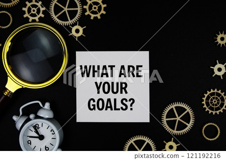 What are Your Goals? text message on sticky note with magnifying glass and alarm clock on black background 121192216