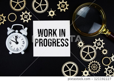Work In Progress text message on sticky note with magnifying glass and alarm clock on black background 121192227