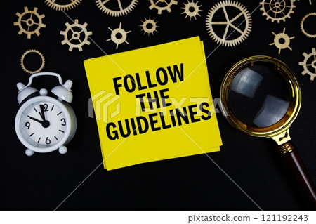 Follow the Guidelines text message on sticky note with magnifying glass and alarm clock on black background 121192243