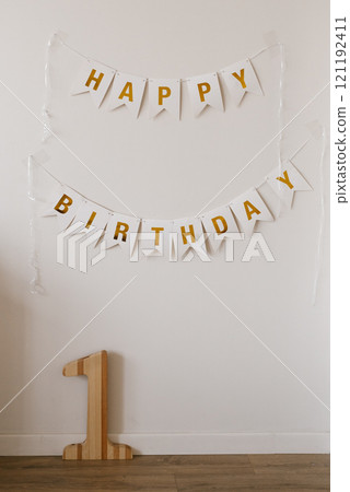 White wall with two banners which says Happy Birthday. Wooden number one on the floor in front of the wall for baby birthday 121192411