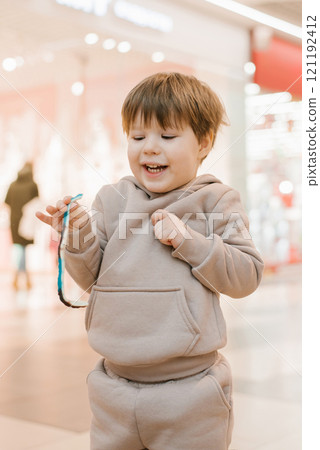 Child boy smiles and holds a blue and white green candy in hands at the mall 121192412