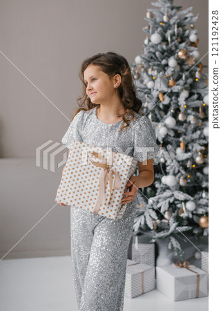 Teenage girl holds gift box in her hands in room decorated for Christmas 121192428