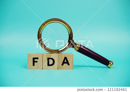 FDA with wooden blocks alphabet letters and Magnifying glass on blue background FDA with wooden blocks alphabet letters and Magnifying glass on blue background 121192481