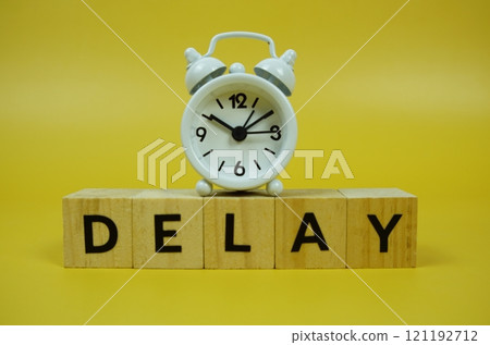 Delay with wooden blocks alphabet letters and alarm clock on yellow background Delay with wooden blocks alphabet letters and alarm clock on yellow background 121192712