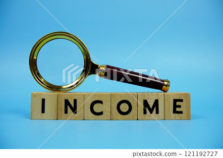 Income with wooden blocks alphabet letters and Magnifying glass on blue background Income with wooden blocks alphabet letters and Magnifying glass on blue background 121192727