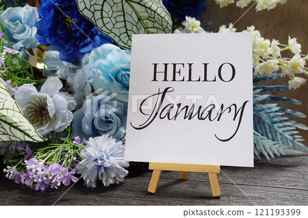 Hello January text write on paper card with wooden easel and flowers decoration on wooden background 121193399