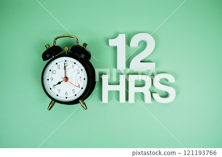 12 Hrs alphabet letters and alarm clock top view on green background 121193766