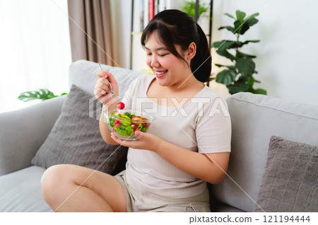 Beautiful Asian woman eating salad, holding a glass bowl and using a fork to pick up a tomato to eat 121194444