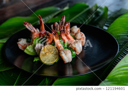 Freshly grilled tiger shrimp beautifully presented on a bed of crisp lettuce and vibrant lime slices, showcasing the culinary artistry typical of Asian cuisine. 121194601