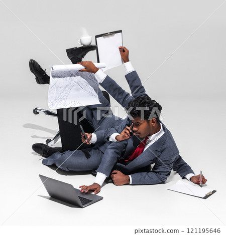 Relentless multitasking demands of corporate life. Businessman in suit balances various office tools, including documents, phone, and laptop Relentless multitasking demands of corporate life. Businessman in suit balances various office tools, including documents, phone, and laptop 121195646