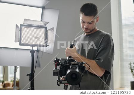 Low angle shot of Caucasian talented operator using professional massive camera at studio Low angle shot of Caucasian talented operator using professional massive camera at studio 121195723