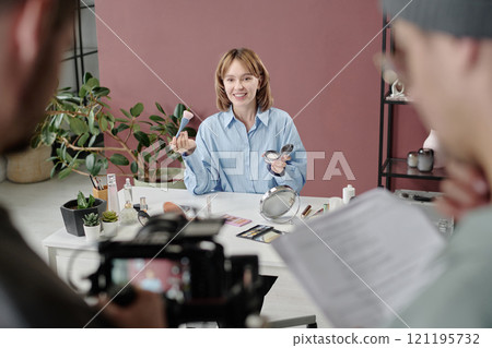 High angle shot of blonde woman demonstrating brush and powder while unrecognizable operator and director watching her play 121195732