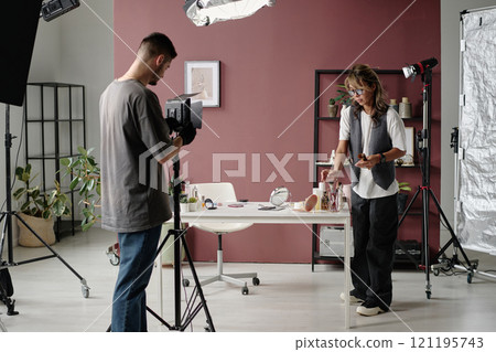 Unrecognizable operator setting lighting kit while his colleague checking props on table before shooting Unrecognizable operator setting lighting kit while his colleague checking props on table before shooting 121195743