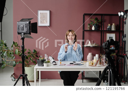 High angle of blonde woman advertising cosmetic products and sitting at table, she surrounded with lighting kit and cameras High angle of blonde woman advertising cosmetic products and sitting at table, she surrounded with lighting kit and cameras 121195766
