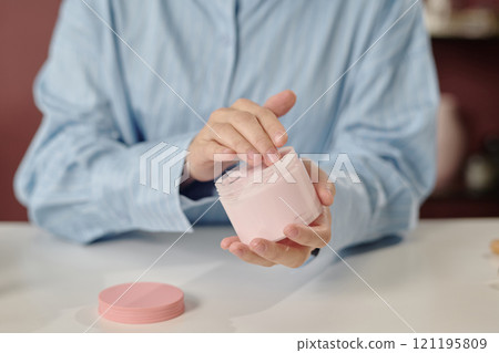 Medium close up of female hands holding big jar of body butter and testing its texture Medium close up of female hands holding big jar of body butter and testing its texture 121195809