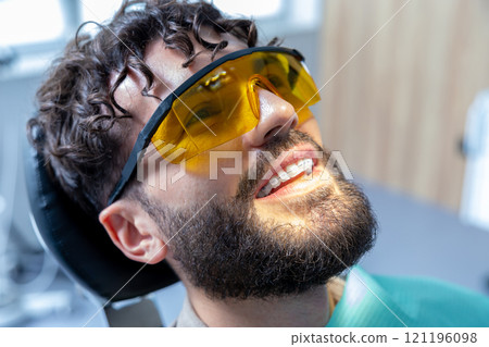 Man in protective glasses in dentist chair having teeth care procedures 121196098